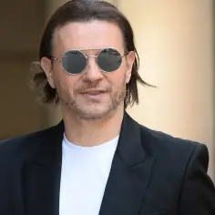 Radosław Majdan w okularach przeciwsłonecznych, z charakterystycznymi, lekko falowanymi włosami i zarostem.