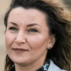 Monika Pawłowska, wiek ok. 40 lat, z burzą brązowych włosów, w jasnej marynarce.