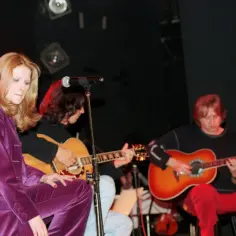 Stanisław Żybowski, mimo choroby, gra na gitarze z zespołem. Wokalistka w fioletowym stroju.