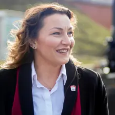 Kobieta w białej koszuli i czarnym płaszczu, uśmiechnięta, patrzy w bok.