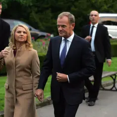 Donald Tusk i jego żona idą trzymając się za ręce, otoczeni przez ochronę.