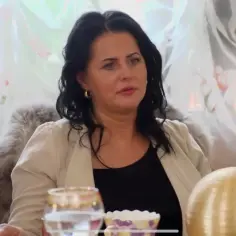 Edzia, królowa życia, w eleganckim żakiecie, siedzi przy stole.