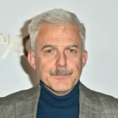 Hubert Urbański z siwymi włosami i wąsami, w szarym garniturze i granatowym golfie. W tle logo "Mój".