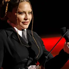 Madonna, w czarnym garniturze i z warkoczami, trzyma mikrofon i biczyk. Pytanie "czy Madonna żyje" nabiera nowego znaczenia.