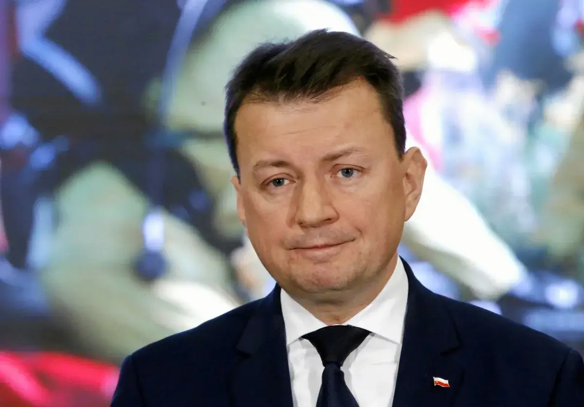 Mężczyzna w garniturze, z przypinką z polską flagą. Nie wiadomo, ile lat ma błaszczak, ale wygląda na dojrzałego.