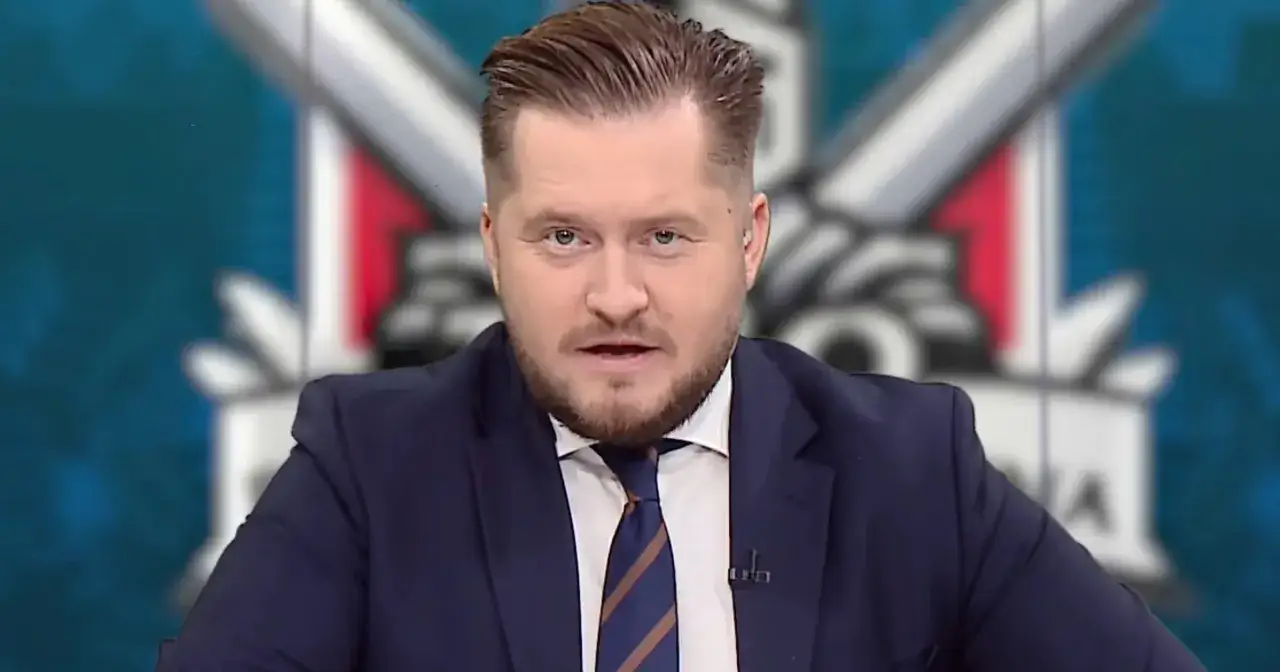 Michał Jelonek, dziennikarz w granatowym garniturze, przemawia na tle logo.
