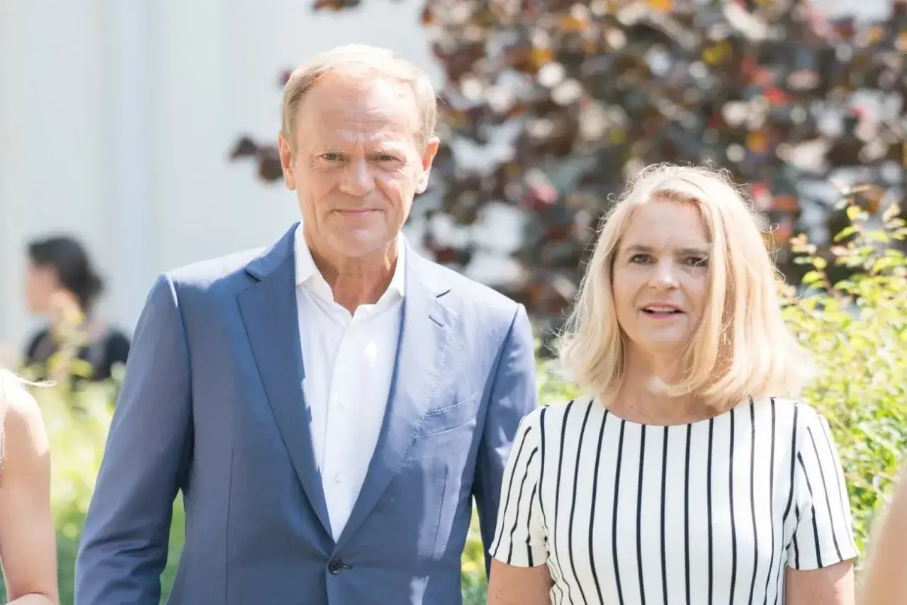 Donald Tusk z żoną Agatą. W tle widać inne osoby i zieleń.
