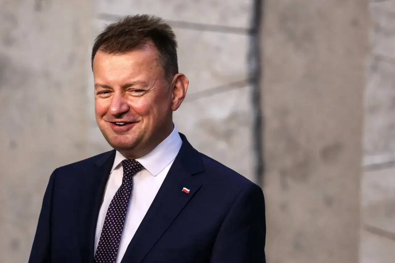Uśmiechnięty mężczyzna w garniturze, z przypinką z polską flagą. Ciekawe, ile lat ma Błaszczak, że tak promienieje?