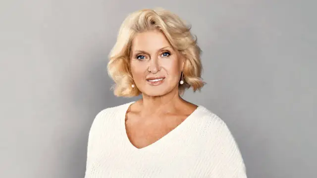 Uśmiechnięta Ewa Kasprzyk w białym swetrze. Wiele osób zastanawia się, ile lat ma Ewa Kasprzyk, ale jej wiek nie wpływa na jej energię.